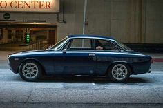 an old blue car is parked in front of a building