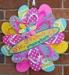 a colorful flip flop wreath hanging on a brick wall with the words it's beach time somewhere