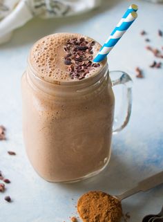 a chocolate smoothie in a mason jar with a blue and white striped straw is next to a cookie