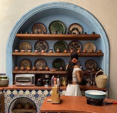 a woman standing in front of a shelf filled with plates