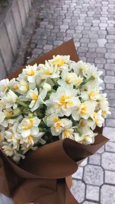 a bouquet of white and yellow flowers sitting in a brown paper bag on the sidewalk