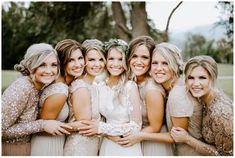 a group of women standing next to each other in front of a tree with their arms around each other