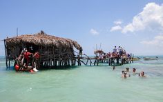 people are swimming in the ocean near a hut on stilts that is built into the water