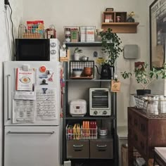 a kitchen area with a refrigerator, microwave and shelves filled with various items on top of it