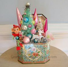 a small christmas tree in a tin can on a table with other ornaments around it