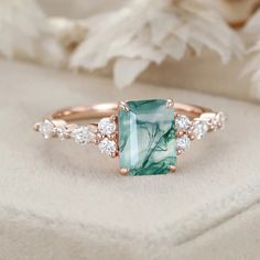 a green and white stone ring with diamonds on the side, sitting on a piece of cloth