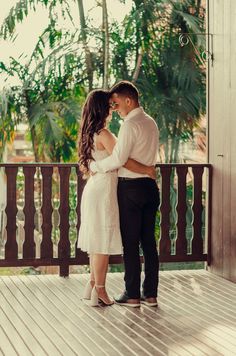 a man and woman standing next to each other on a wooden deck with palm trees in the background