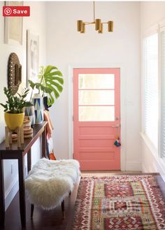 a bright pink door in a white room with an area rug on the floor and potted plants next to it