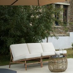 a wicker couch and coffee table with an umbrella in the back yard, next to a brick building