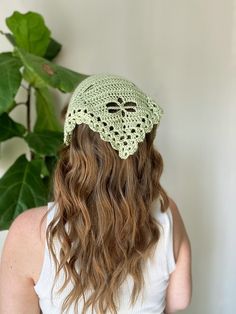 a woman wearing a green crochet hat in front of a potted plant