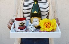 a woman holding a tray with a bottle of wine and two mugs