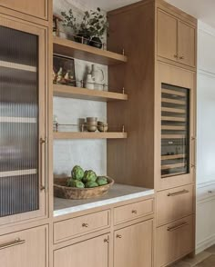 a kitchen with wooden cabinets and shelves filled with green vegetables on the counter top next to a bowl of broccoli