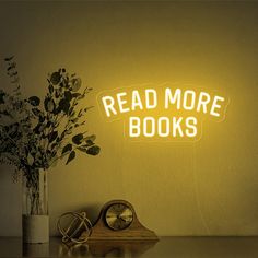 a neon sign that reads read more books next to a vase with flowers in it