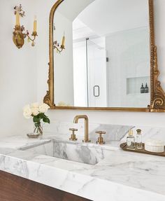 a bathroom sink with marble counter top and gold faucet, mirror above it