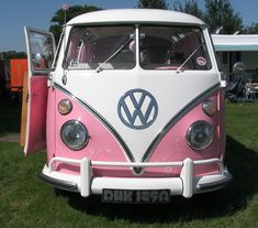 a pink and white vw bus parked in the grass