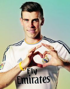 a man making a heart with his hands while standing in front of a green and yellow background