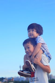 two young boys standing next to each other with their arms around one another and the sky in the background