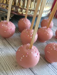 pink cake pops with sprinkles and wooden skewers on a table