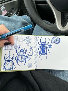 a person is holding a notebook with blue drawings on it and a pen in their hand