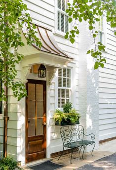 a white house with an iron bench and potted plants on the front door porch