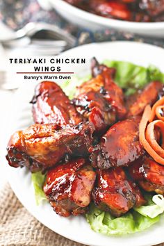 two plates with chicken wings and carrots next to each other on top of lettuce