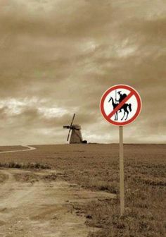 a black and white photo of a sign in the middle of a field with windmills behind it