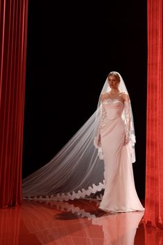 a woman in a white wedding dress and veil standing between two red pillars with curtains behind her