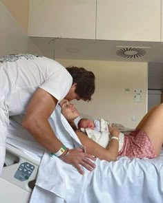 a man and woman are looking at a baby in a hospital bed while the child is being held up by an adult