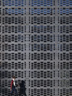 two people walking in front of a building made out of metal grates and bricks