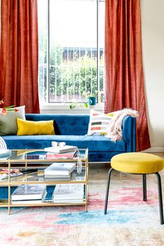 a living room filled with furniture and a window covered in red draping next to a blue couch