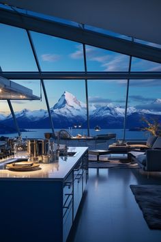 a kitchen with an island counter and large windows overlooking the mountains in the evening time