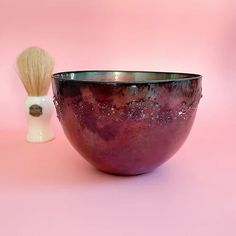 a purple bowl with a white shaving brush in it sitting on a pink surface