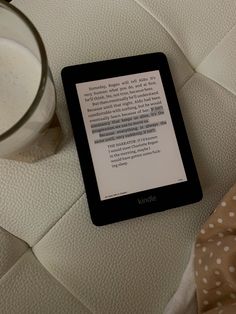 the kindle is next to a glass of milk