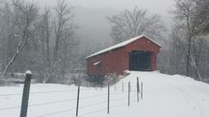 a red barn sitting on top of a snow covered hill next to a fence and trees