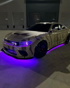 a camo car with purple lights on the hood is parked in front of a garage