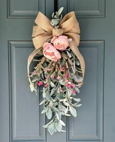 a wreath with pink flowers hanging on the front door and an olive colored bow tied to it