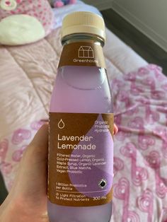 a bottle of lavender lemonade in someone's hand on a pink bedspread