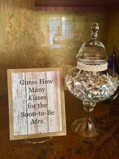 there is a glass bowl with candy in it next to a sign that says guess how many kisses for the son - to - be mrs