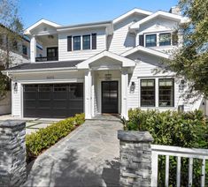 a white house with black garage doors and two story windows on the front of it