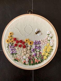 an embroidery project with flowers and a bee in the middle is hanging on a wall