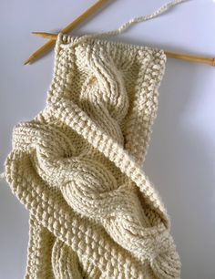 a white knitted blanket sitting on top of a table next to two knitting needles