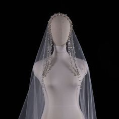 a white wedding veil with crystal beading on the top and bottom, in front of a mannequin's torso