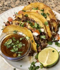 some tacos are on a plate with sauce and cilantro next to it