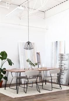 a dining room table and chairs with plants on the floor in front of white walls