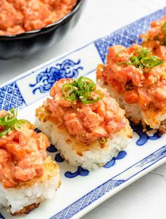 four pieces of sushi on a blue and white platter with a bowl of sauce in the background