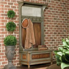 a wooden bench with a hat and coat on it next to a potted plant