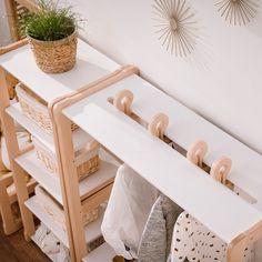 a white shelf with clothes hanging on it and a potted plant next to it