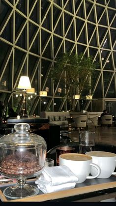 two cups of coffee sit on a table in front of a large glass building with windows