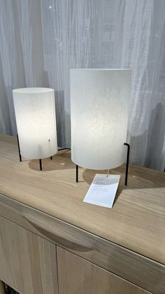 two lamps sitting on top of a wooden dresser next to a sheet of white paper