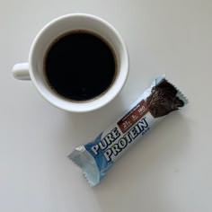 a cup of coffee next to a bar of chocolate on a white counter top with the word pure protein in it